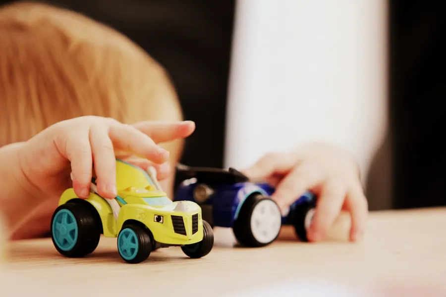 Ilustrasi mimpi anak kecil — child playing with two assorted-color car plastic toys on brown wooden table