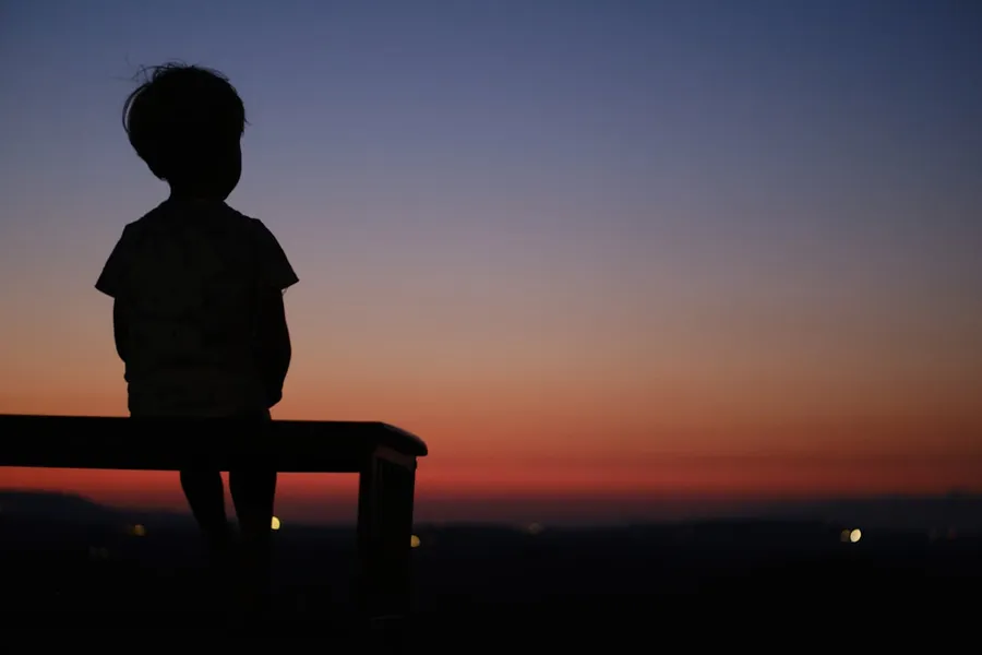Ilustrasi mimpi anak sakti — a silhouette of a child sitting on a bench