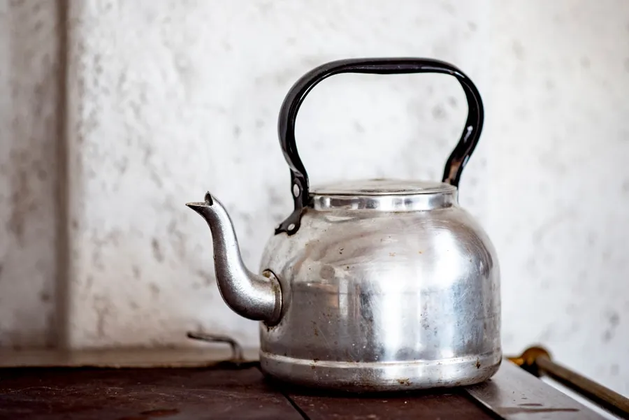 Ilustrasi mimpi ceret — stainless steel kettle on brown wooden table