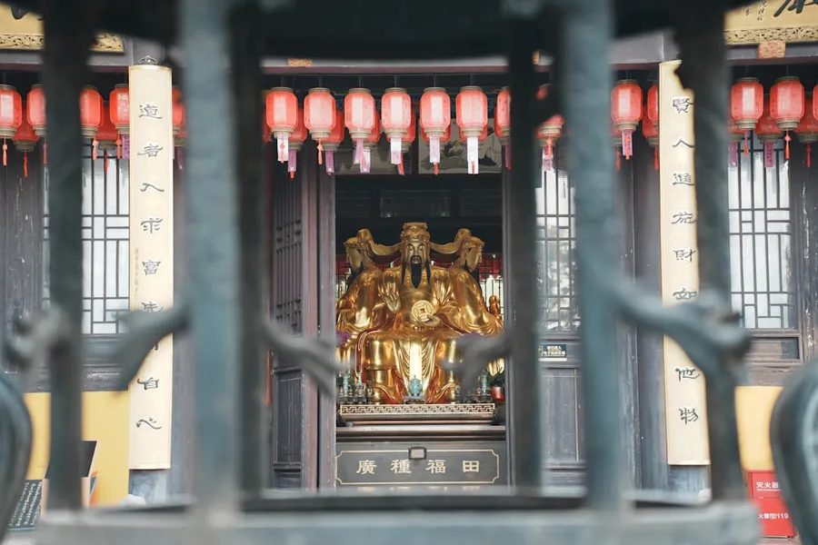 Ilustrasi mimpi dewa uang — Golden statue inside a temple with red lanterns.
