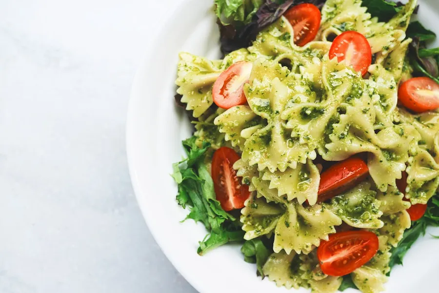 Ilustrasi mimpi makan — Pesto pasta with sliced tomatoes served on white ceramic plate