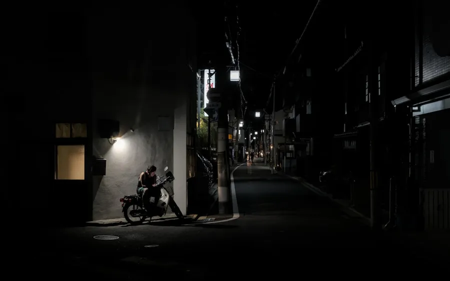 Ilustrasi mimpi pembunuh — Motorcycle parked on dark, narrow street at night.