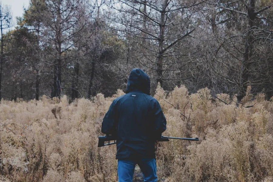 Ilustrasi mimpi pemburu — man in black jacket and blue denim jeans standing on brown grass field during daytime