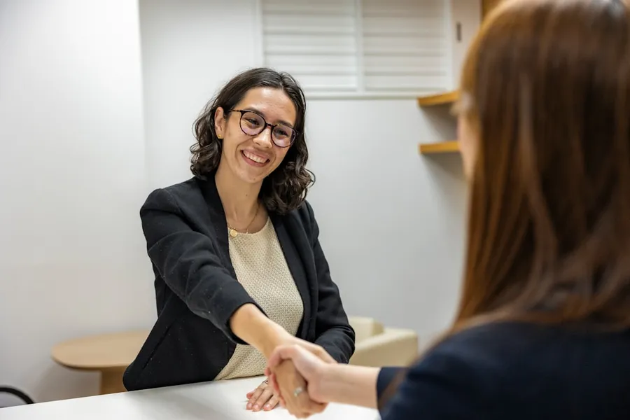 Ilustrasi mimpi penjilat — a woman shaking hands with another woman sitting at a table
