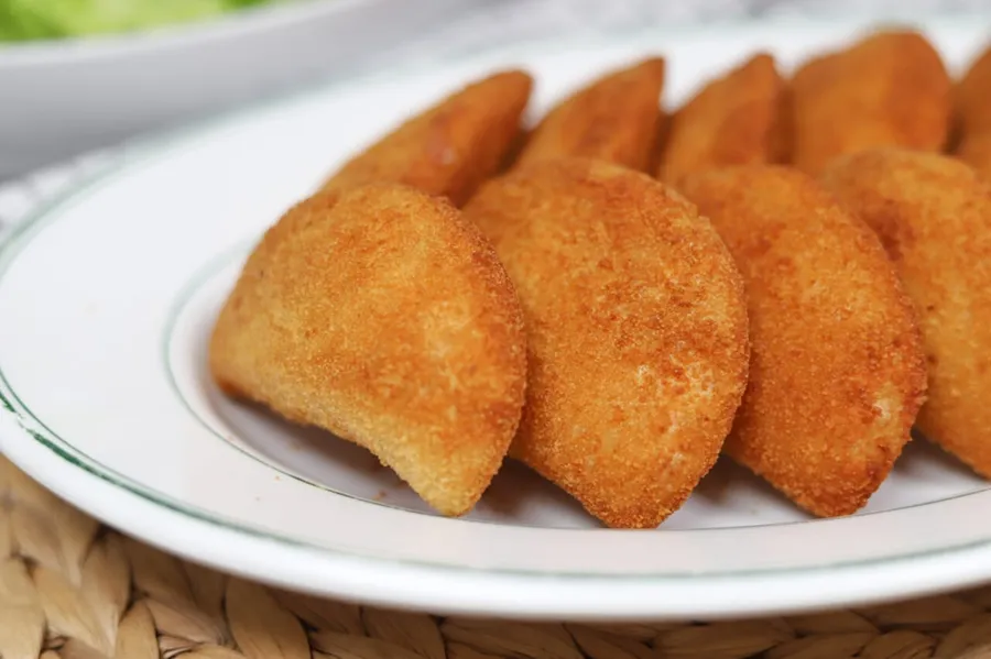 Ilustrasi mimpi risol — Golden brown empanadas arranged on a white plate.